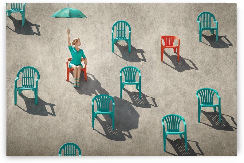 Young blonde woman holding up a turquoise umbrella on a beach sitting through many red and teal chairs in the sand on a sunny day by Artmood Visualz