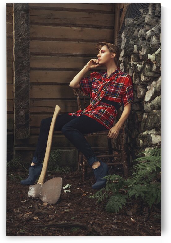 Young beautiful woman with short hair wearing a long plaid shirt sitting on a chair outside of a shack with an antique axe leaning against her leg by Artmood Visualz