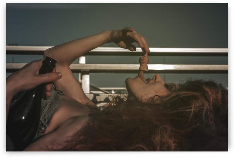 Vintage portrait of a tipsy beautiful young woman wearing an old school denim dress and long teased hair celebrating alone with champagne in the bleachers of a soccer field by Artmood Visualz