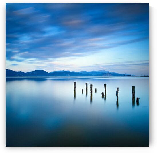Wooden pier remains on a blue lake. Italy by Stefano Orazzini