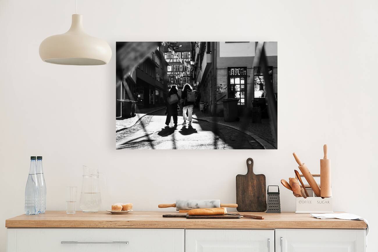 Black and white street photo of people walking down the road seen through the spokes of a bicycle Reproduction