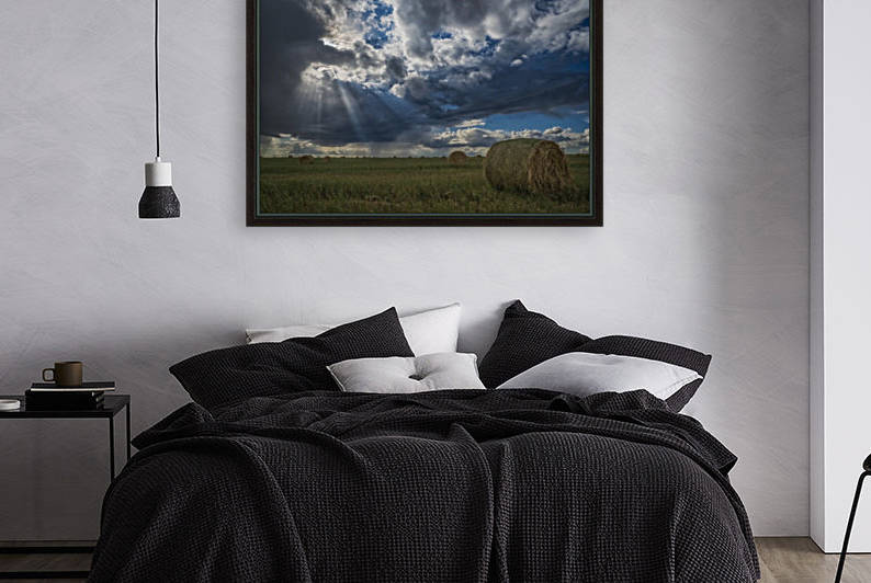 Sunlight breaks through the storm clouds over a field of hay bales; Saskatchewan, Canada by PacificStock