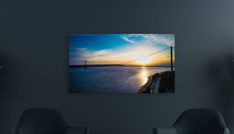 Sunset view over a calm river with a silhouette of a suspension bridge against a colorful sky in Hull England. by Vasile Jechiu