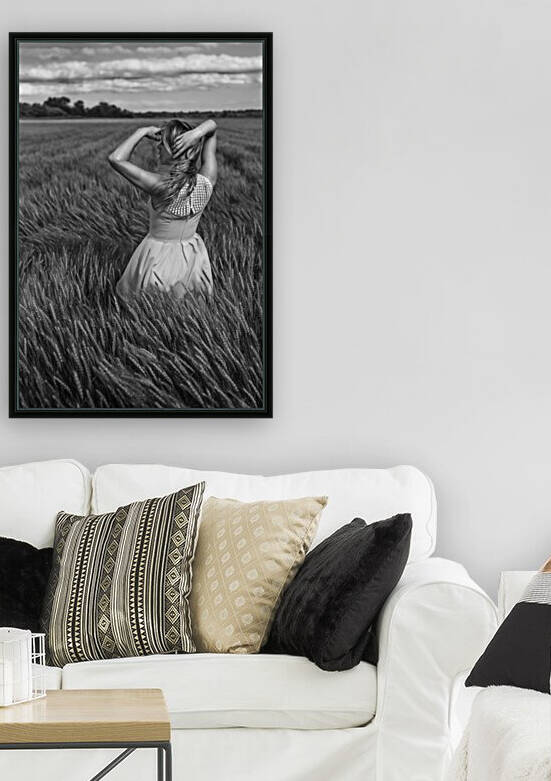 Black and white portrait of a beautiful young woman wearing a summer dress her blonde hair floating in the wind standing outdoors in a wheat field on a cloudy day by Artmood Visualz