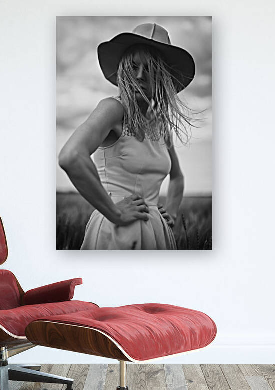 Black and white portrait of a beautiful young woman wearing a summer dress and a sun hat standing outdoors in a wheat field on a cloudy day by Artmood Visualz