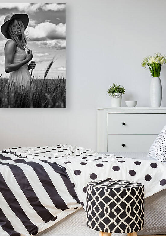 Black and white portrait of a beautiful young woman wearing a summer dress and a sun hat standing outdoors in a wheat field on a cloudy day by Artmood Visualz