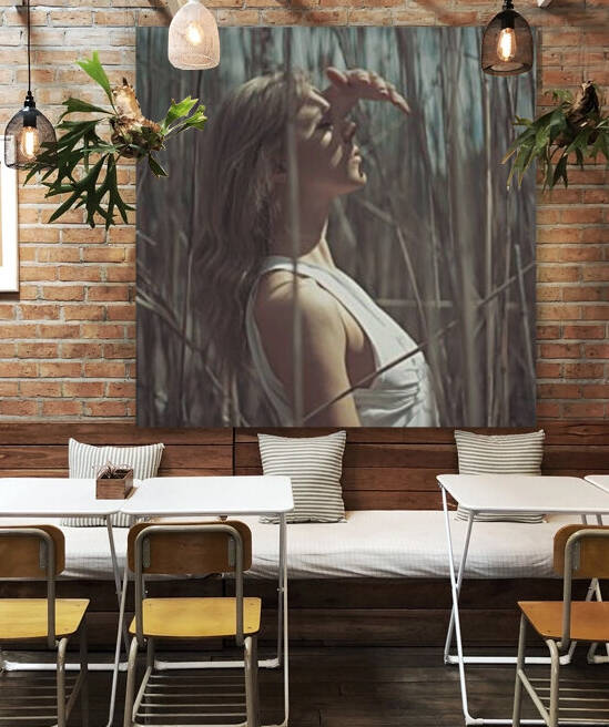 Beautiful young blonde woman wearing a white summer dress standing in a field of reeds blocking the sun with her hand by Artmood Visualz