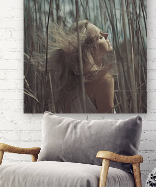 Beautiful young blonde woman wearing a white summer dress standing in a field of reeds her eyes closed and her hair twirling around by Artmood Visualz