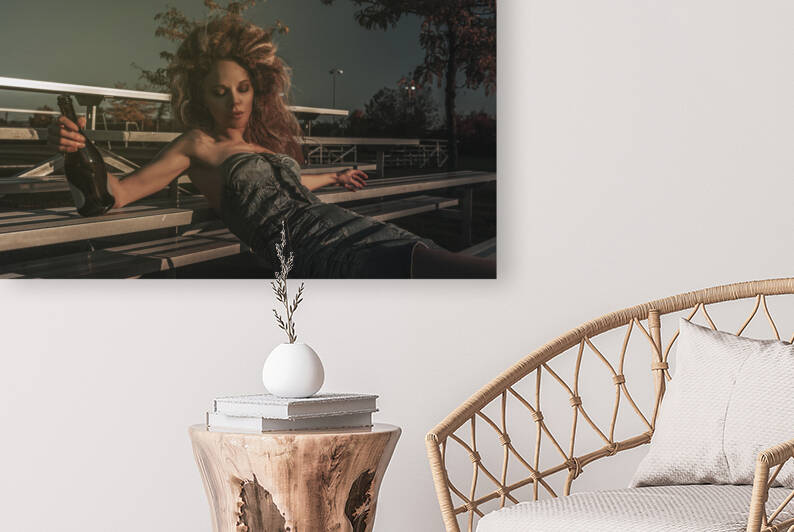 Vintage portrait of a tipsy beautiful young woman wearing an old school denim dress and long teased hair celebrating alone with champagne in the bleachers of a soccer field by Artmood Visualz